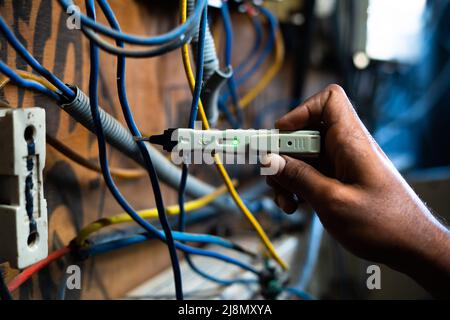 Gros plan de l'électricien vérifiant le flux de courant à l'aide d'un testeur de tension de continuité sur la carte de circuit imprimé - concept de technologie, de réparation et de maintenance Banque D'Images