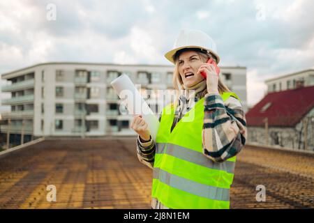 Femme en colère ouvrier de construction dans casque avec smartphone extérieur vérifiant la construction. Concept de l'industrie Banque D'Images