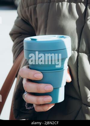 Les mains des femmes tiennent une tasse à café réutilisable bleue. Style de vie durable. Concept écologique. Banque D'Images