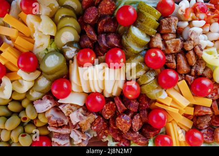 tomates cerises, poivrons doux, concombres marinés, ail mariné, olives, saucisse, différents fromages, bacon sur une assiette en bois. En-cas Banque D'Images