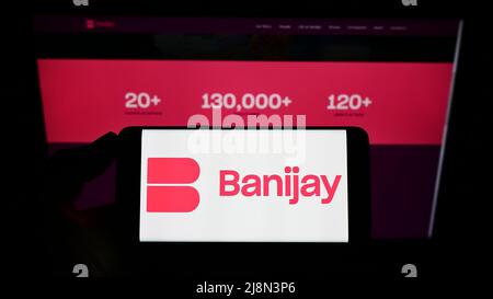 Personne tenant un téléphone portable avec le logo de la société française de divertissement Banijay Group à l'écran en face de la page web. Mise au point sur l'affichage du téléphone. Banque D'Images