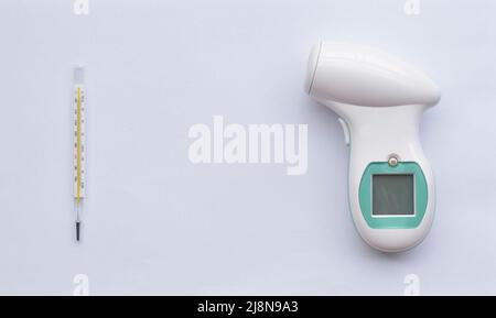 Comparaison entre un thermomètre en verre au mercure et un thermomètre numérique frontal infrarouge sans contact. Isolé sur blanc. Banque D'Images