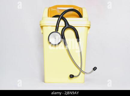 Stéthoscope noir dans une petite poubelle en plastique jaune. Montre Quitter l'emploi médical, décevoir et abandonner la profession de docteur. Banque D'Images