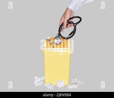 Médecin écartant le stéthoscope noir dans une petite poubelle en plastique jaune. Montre Quitter l'emploi médical, décevoir et abandonner la profession de docteur. Banque D'Images