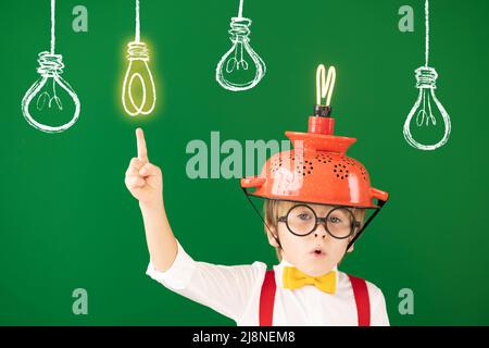 Enfant intelligent dans la classe contre le tableau noir. Enfant drôle avec une ampoule à l'école. Concept d'éducation, de démarrage et d'idée d'entreprise Banque D'Images