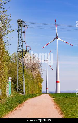 D'énormes éoliennes et des pylônes d'électricité pour produire de l'électricité verte se trouvent à côté d'une route de terre dans les zones rurales de l'Allemagne Banque D'Images