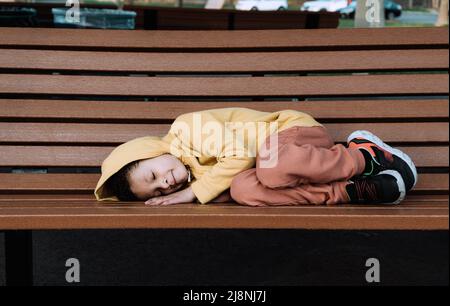 Triste seul, un petit garçon se repose sur un banc dans un parc public. Espace-copie Banque D'Images