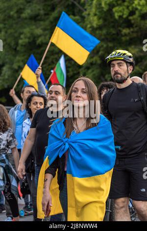 Une femme avec un regard décisif, enveloppée dans un drapeau ukrainien, marche dans une foule à la manifestation d'aide Ukraine Banque D'Images