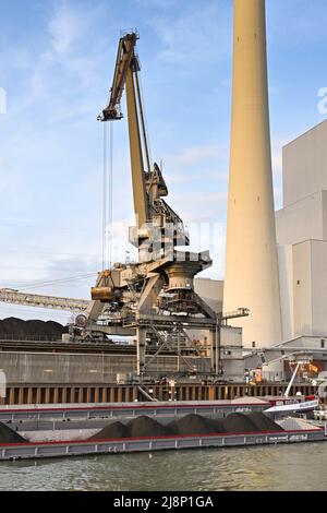 Mannheim, Allemagne - avril 2022 : grue déchargeant du charbon d'une barge industrielle dans une centrale électrique sur le Rhin. L'usine est exploitée par CKM. Banque D'Images