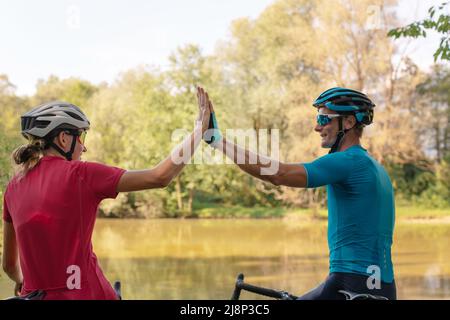 Femme et homme, les cyclistes professionnels de course de route de haut cinq les uns les autres et de détente sur un rivage de rivière Banque D'Images