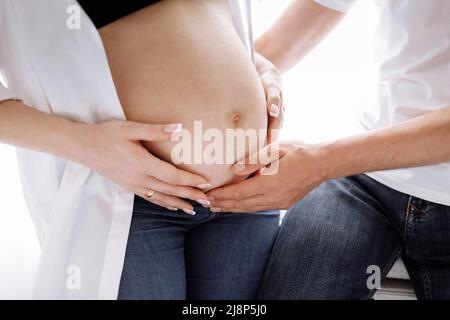 Photo rognée d'un couple enceinte à la maison, l'homme est embrassant et touchant la femme grand ventre. Grossesse, parentalité, amour, concept de famille. Photo de haute qualité Banque D'Images