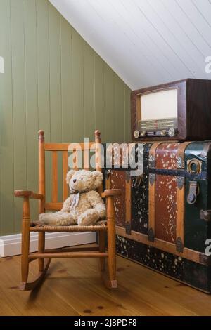 Chaise à bascule antique avec ours en peluche et radio sur le dessus de coffre de rangement dans la chambre d'hôtes à l'intérieur de la vieille maison de style Canadiana vers 1866. Banque D'Images