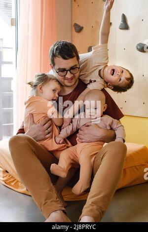 Père heureux avec arbre petits enfants jouant à la maison. Papa câlin avec les enfants, en les tenant sur les mains. Amusez-vous en grande famille, jour ensoleillé. Papa tout porter Banque D'Images