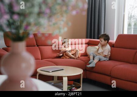 Frère et sœur assis sur le canapé. Frères et sœurs communiquant à la maison, jouant ensemble. Famille de style de vie. Vue sur les fleurs dans un vase. Moderne Banque D'Images