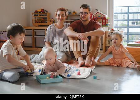 Grande famille dans une salle de jeux ensoleillée. Parents jouant avec des enfants et des jouets. Joyeux temps avec les jeux. Mère père fils filles dans une maison moderne colorée Banque D'Images