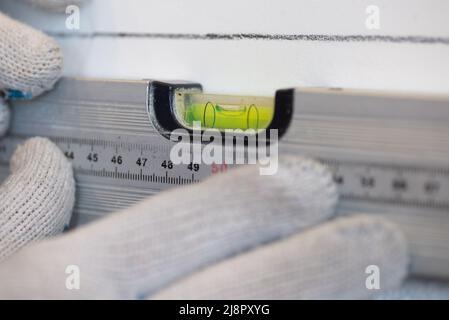 Les mains du travailleur vérifient la planéité du mur à l'aide d'un outil spécial pour mesurer le niveau. La scène de face au mur de la cuisine avec des carreaux de céramique blanche Banque D'Images