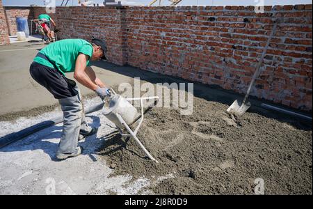 Travailleur masculin utilisant un mélangeur de table en béton lors de la préparation du mélange sable-ciment pour la table de plancher. Homme de construction travaillant avec un équipement professionnel de table de plancher sur le chantier de construction. Banque D'Images