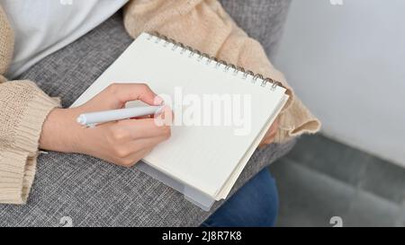 Femme prenant des notes sur le bloc-notes en spirale, écrivant à la main quelque chose sur du papier vierge, notant la liste sur le bloc-notes ou écrivant un journal intime. Rogné Banque D'Images