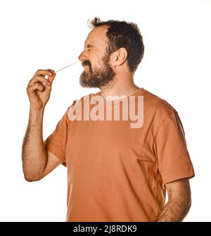 homme barbu effectuant un test d'antigène avec expression désagréable. sur fond blanc isolé pour la publicité. Mal à l'aise lors du test. Banque D'Images