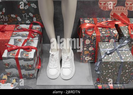 Mannequin féminin en baskets blanches au milieu des boîtes-cadeaux. Décoration de Noël. Achats de vacances. Banque D'Images