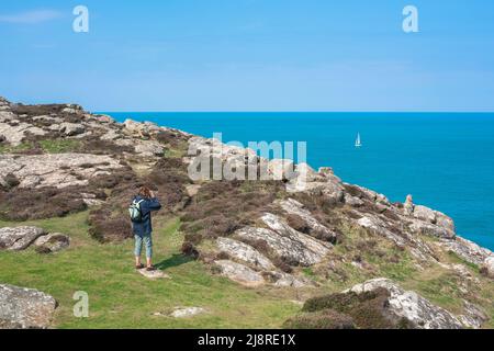 St David's Head pays de Galles, vue en été d'une randonneur femelle sur St David's Head, regardant un yacht éloigné naviguant sur la côte du Pembrokeshire, pays de Galles Banque D'Images