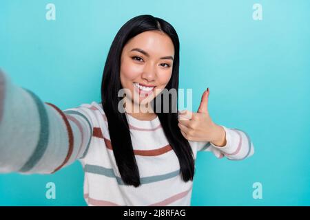 Photo de charme décontracté jeune blogueur influenceur prendre selfie montrant le pouce-vers le haut isolé sur fond de couleur sarcelle Banque D'Images