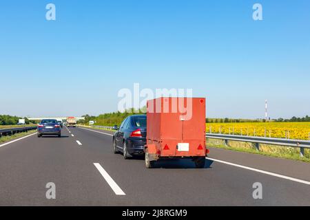 Voiture noire avec remorque de chargement rouge sur la route Banque D'Images