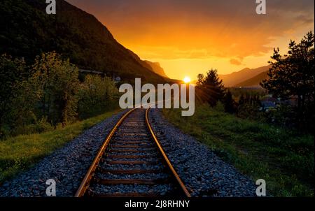 Voies de chemin de fer menant à un beau coucher de soleil avec des nuages sombres au-dessus. La fin d'une trajectoire. Banque D'Images