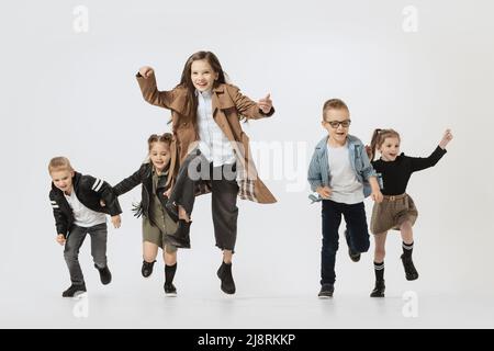 Emotive école et enfants d'âge préscolaire, filles et garçons courant, sautant isolé sur fond gris studio. Beauté, mode pour enfants, éducation Banque D'Images