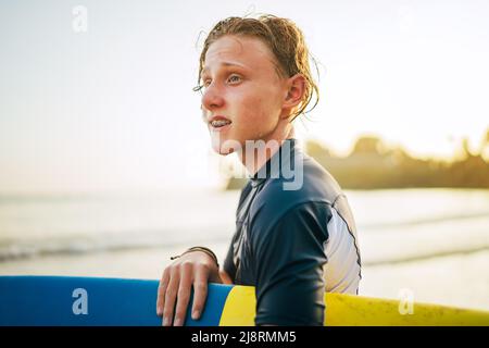 Portrait d'un jeune garçon avec des bretelles dentaires et des cheveux mouillés avec une planche de surf va pour le surf. Il sourit et marche dans l'eau. Bonne enfance et Banque D'Images