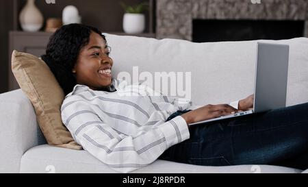 Fille émotionnelle africaine femme américaine regardant un ordinateur portable allongé sur un canapé à la maison se sent enchantée surprise choc merveille lectures bonne nouvelle reçoit avis wi Banque D'Images
