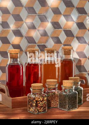 Quatre bouteilles de thé froid aux fruits, rooibos, vert et noir, avec quatre pots de thés séchés, dans un plateau en bois sur une table en bois Banque D'Images