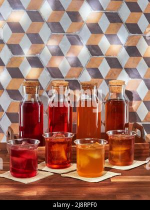 Quatre bouteilles et quatre verres de thé aux fruits, rooibos, vert et noir, dans un plateau en bois sur une table en bois Banque D'Images