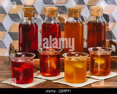 Quatre bouteilles et quatre verres de thé aux fruits, rooibos, vert et noir, dans un plateau en bois sur une table en bois Banque D'Images