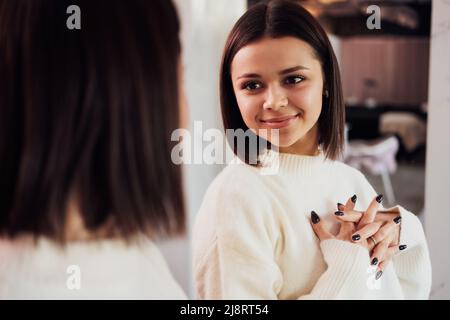 Jeune caucasienne s'admirant dans le miroir dans le couloir du salon de beauté Banque D'Images