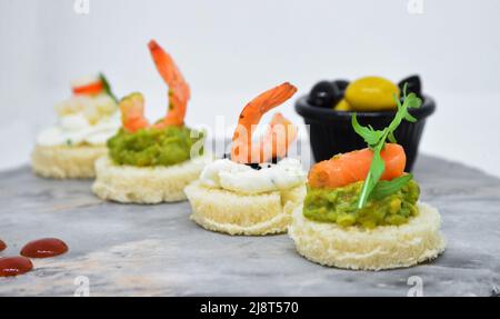 Hors-d'œuvre ou en-cas de crevettes sauschetta à l'avocat avec du pain à grains entiers sur du marbre blanc, vue rapprochée. Crevettes frites et purée d'avocat sur un toaste Banque D'Images