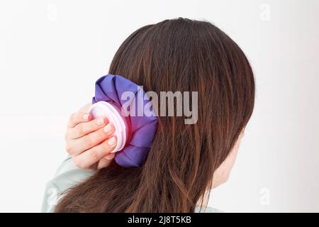 Une fille tient un sac de glace bleu près de sa tête pour éliminer la douleur dans la tête avec des céphalalgies et des ecchymoses Banque D'Images