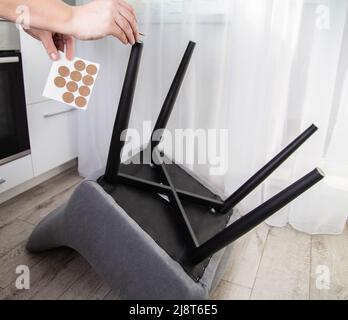 Un homme colle des coussins protecteurs sur les pieds d'une chaise. Protection contre les rayures et le bruit du sol, intérieur Banque D'Images