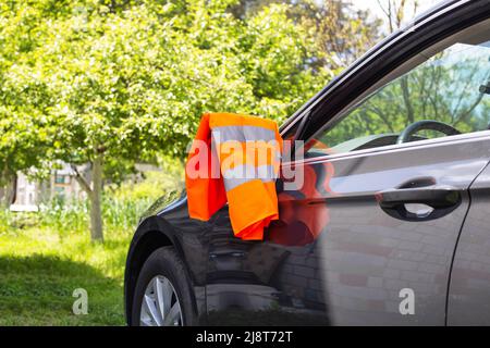 Un gilet d'avertissement orange est suspendu sur le rétroviseur d'une voiture de tourisme. Concept de panne de voiture, signal d'assistance routière, problèmes Banque D'Images