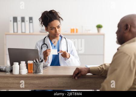 Femme médecin noir montrant des pilules à un patient mâle Banque D'Images