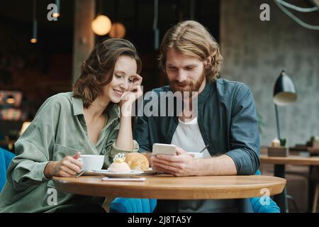 Portrait d'un homme moderne sérieux avec barbe assis à table ronde dans le café loft et appelant par téléphone portable Banque D'Images