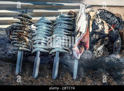 Gros plan du barbecue à poisson sur des brochettes de métal sur des charcoals chauds. Arrière-plan de la rue. Malaga, Andalousie, Espagne Banque D'Images