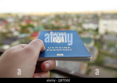 Recentrer le passeport d'un citoyen ukrainien dans une main féminine sur un fond urbain flou, gros plan. Inscription au passeport ukrainien. Guerre. Par Banque D'Images