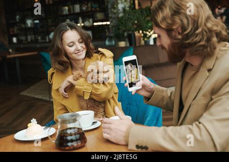 Portrait d'un homme moderne sérieux avec barbe assis à table ronde dans le café loft et appelant par téléphone portable Banque D'Images