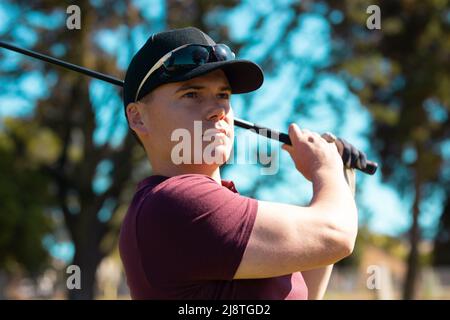 Un jeune homme du Caucase portant des lunettes de soleil et une casquette prenant une balle de golf avec le club en été Banque D'Images