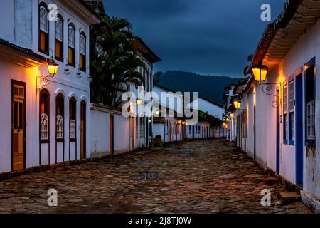 Rues et maisons de la ville historique de Paraty dans l'état de Rio de Janeiro illuminées au crépuscule avec les montagnes en arrière-plan Banque D'Images