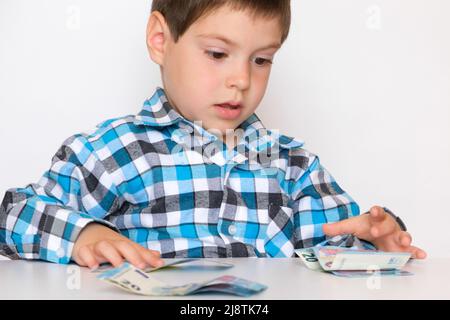 Un garçon de 4 ans compte de l'argent, tient des euros entre ses mains. Enseigner aux enfants la littératie financière, de l'argent de poche. Banque D'Images