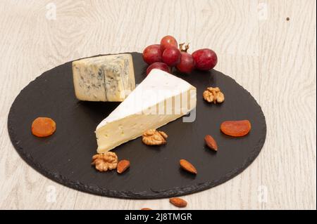 Différents types de fromage sur une planche en graphite avec des noix et des fruits secs Banque D'Images