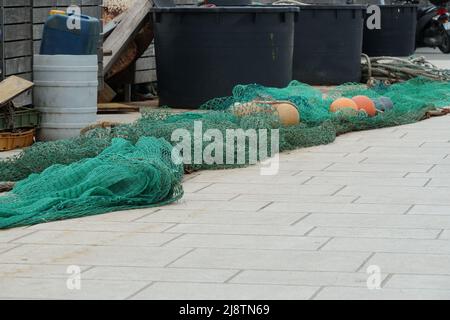 Filet de pêche vert avec flotteurs rouges-bruns étirés sur le pavé carrelé dans le port prêt pour le chargement sur le bateau de pêche. Banque D'Images