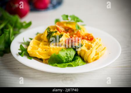 Omelette aux œufs farcie à la tomate et aux légumes verts frits sous forme de gaufres, sur une table en bois. Banque D'Images